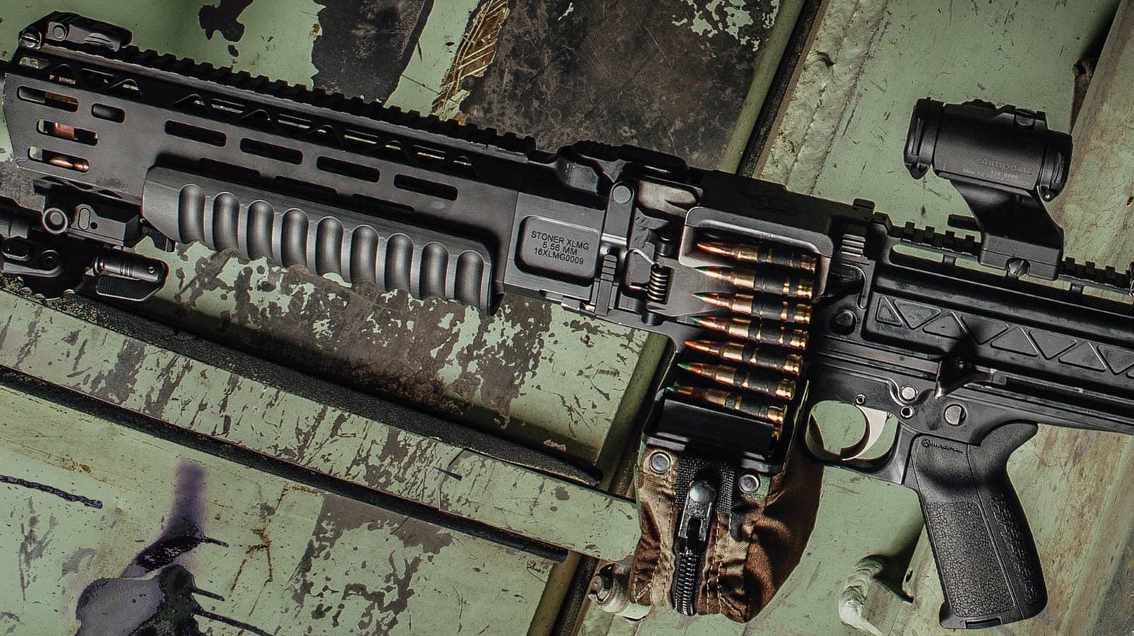 Close view of the LAMG receiver, feed tray and linked ammunition on a weathered green surface