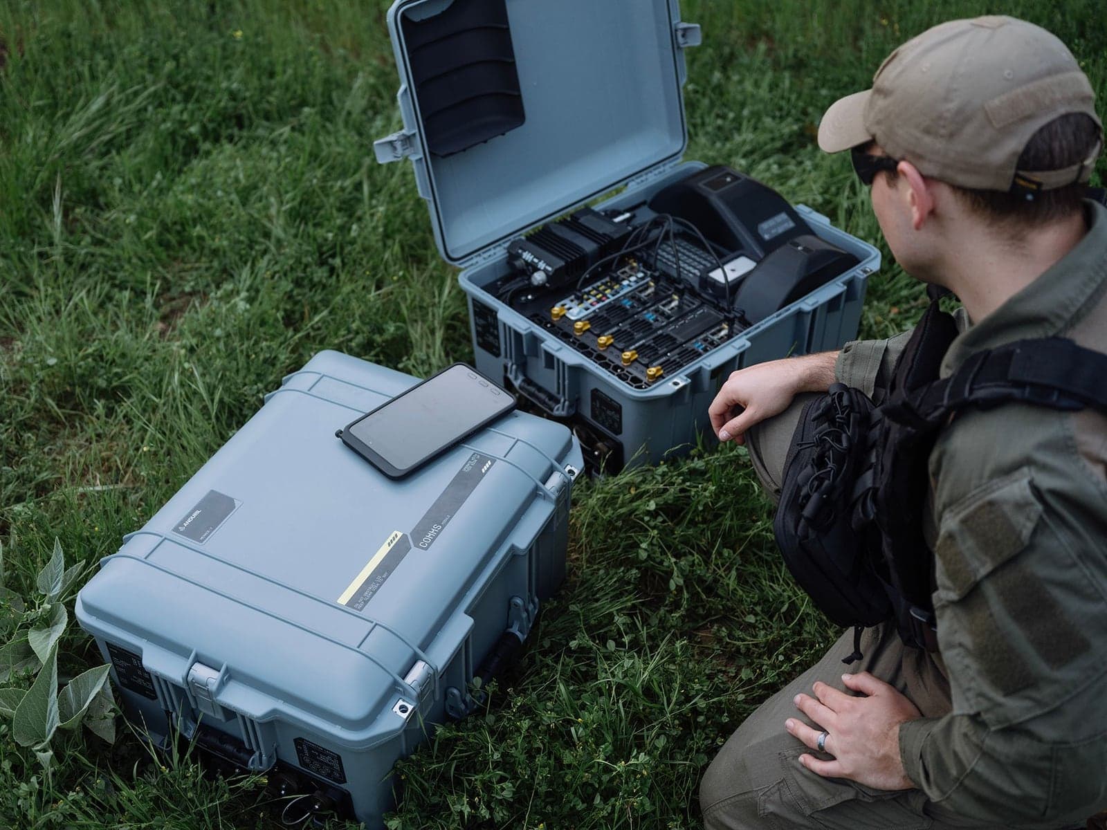 Operator kneeling in a field beside two open Menace-T cases of electronics