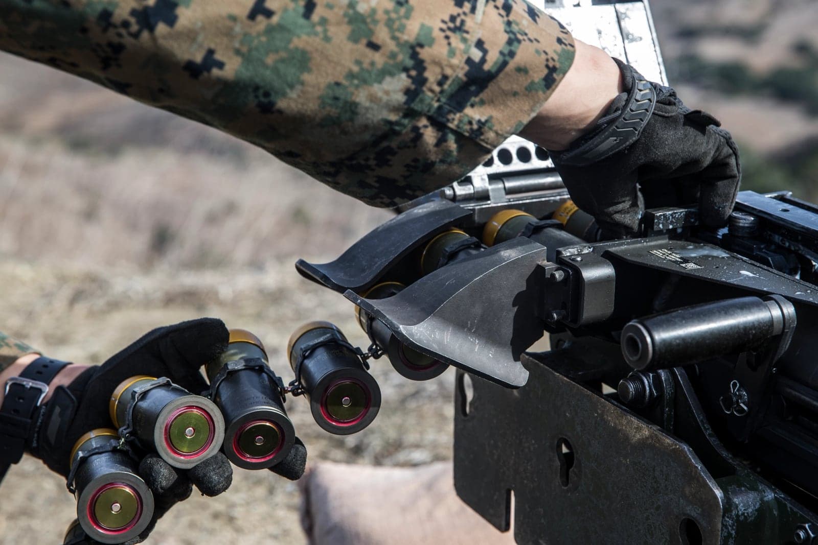 Close view of a Marine loading linked 40mm grenades into a MK19 feed tray