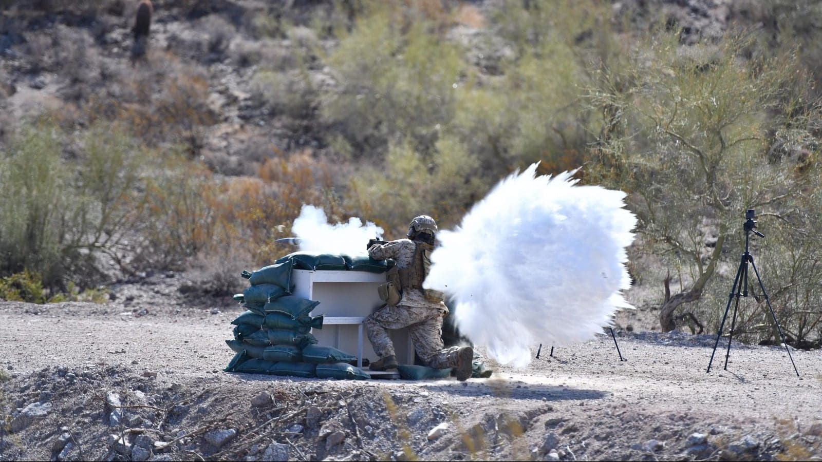 Gunner firing an M72 FFE from a sandbagged enclosure on a desert range, with backblast visible