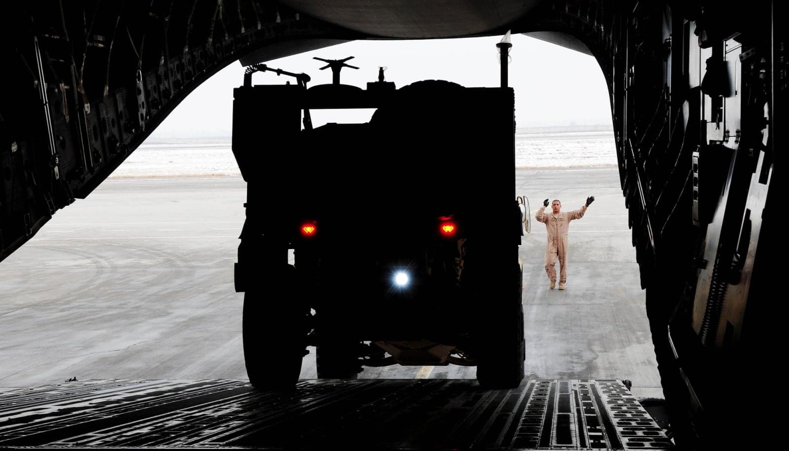 M-ATV silhouetted as a loadmaster guides it into a C-17 cargo hold