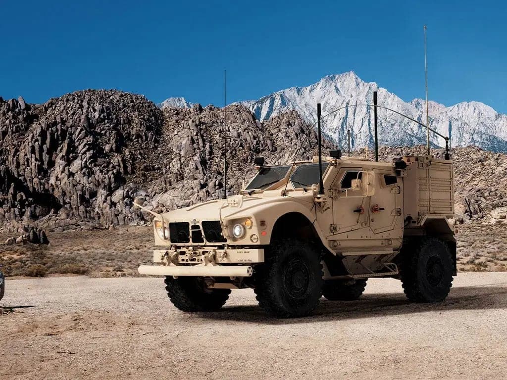 Tan Oshkosh M-ATV special forces variant parked on a desert plain below snow-capped mountains